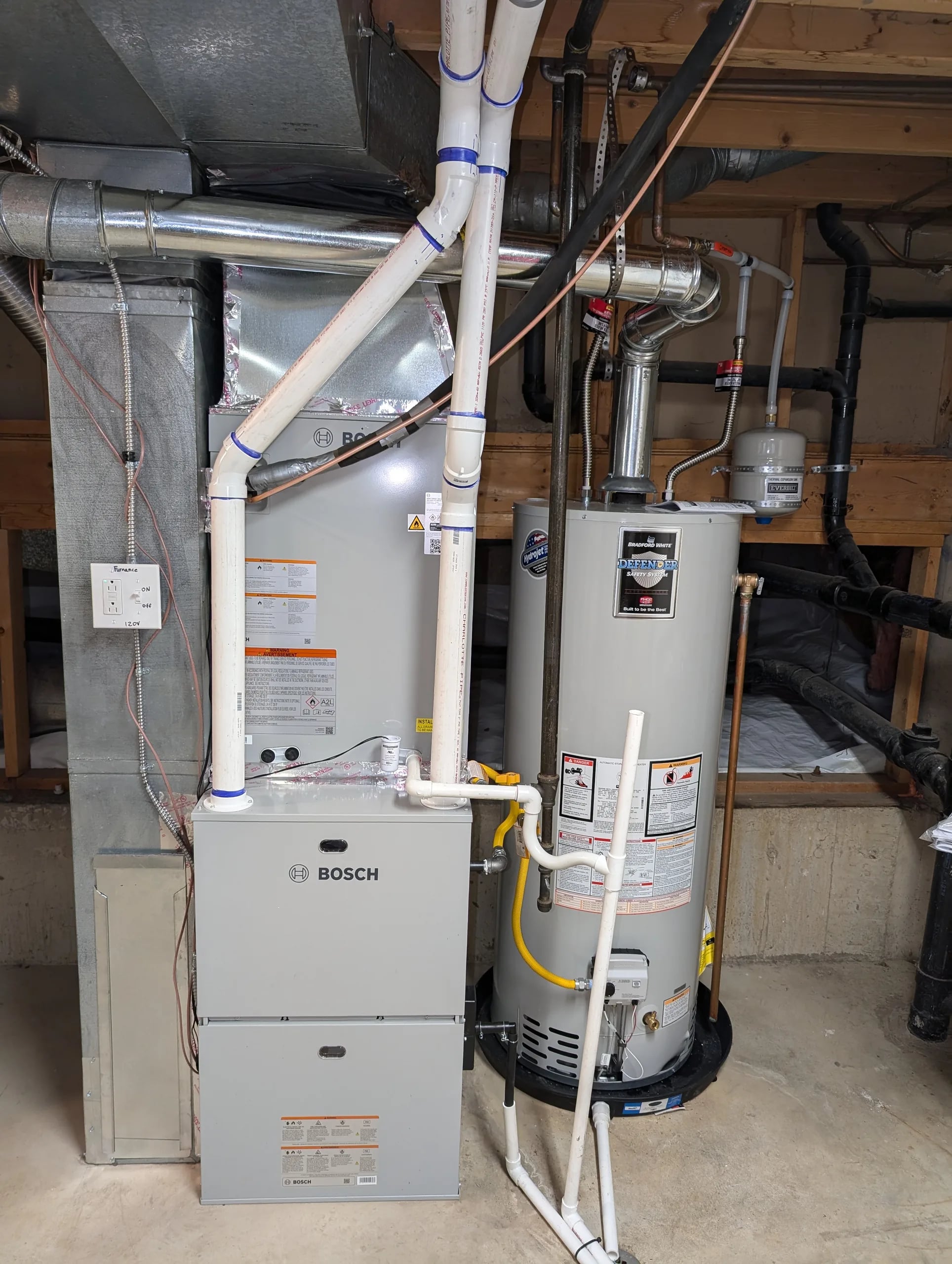 Bosch gas furnace with its coil cabinet above and white PVC pipes, beside a Rheem water heater in a basement