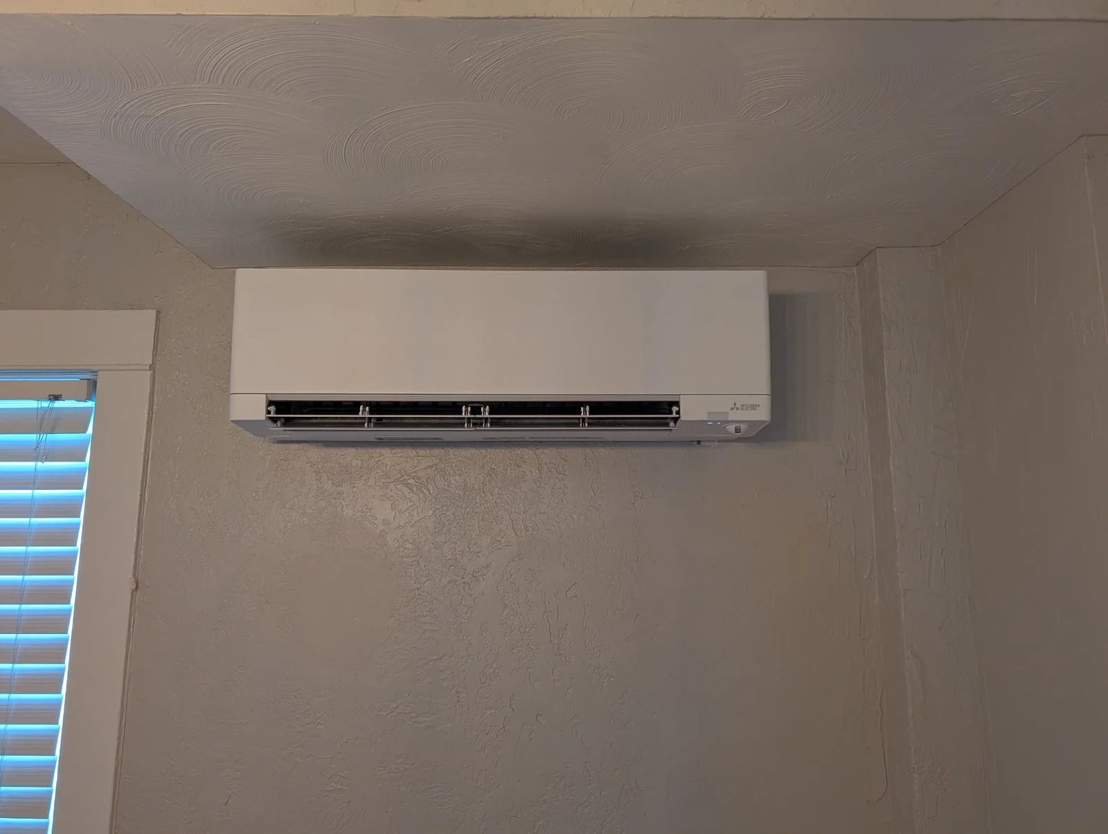A ductless head near the ceiling beside a window with blinds