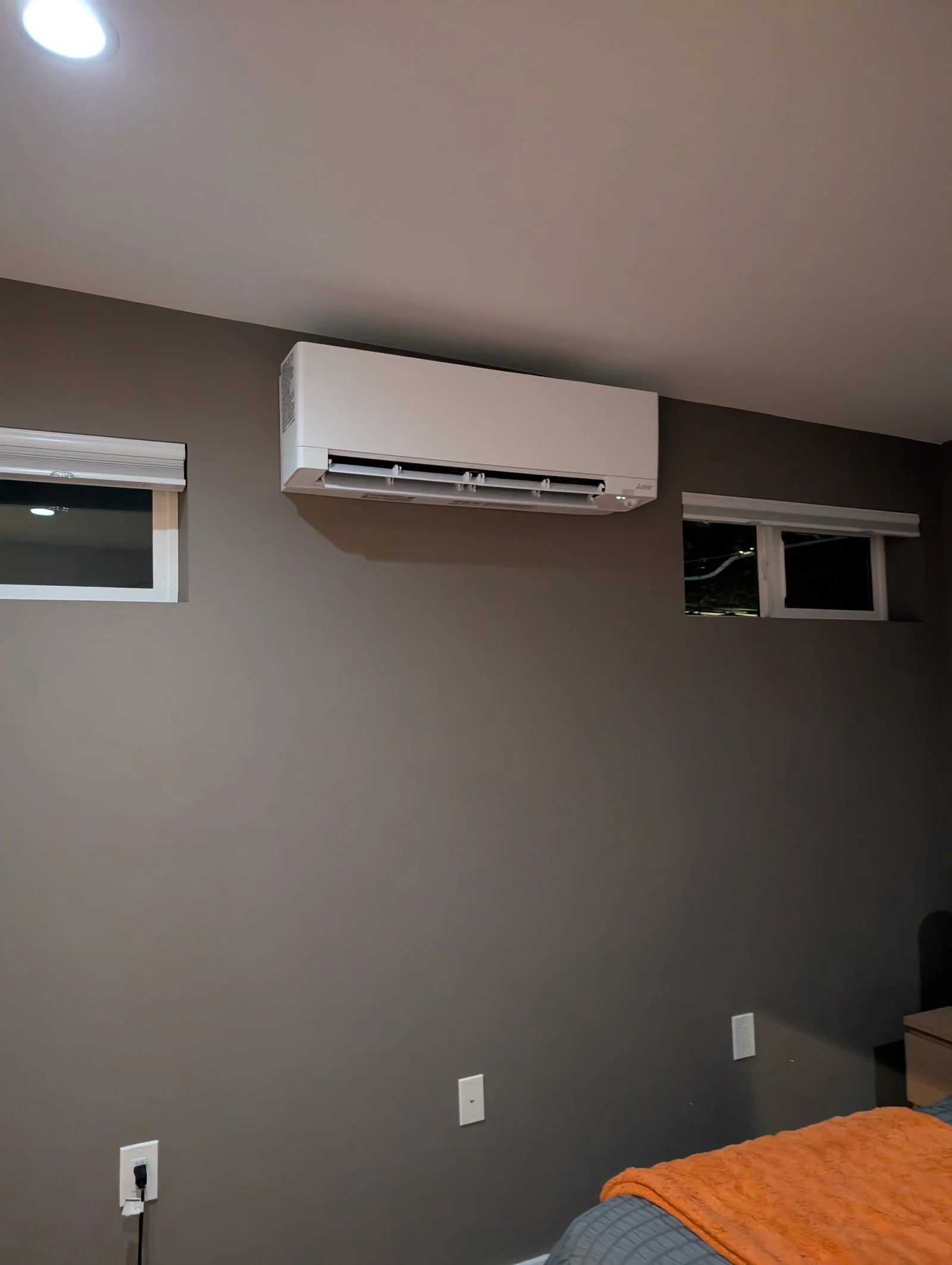 A ductless head high on a bedroom wall between two windows
