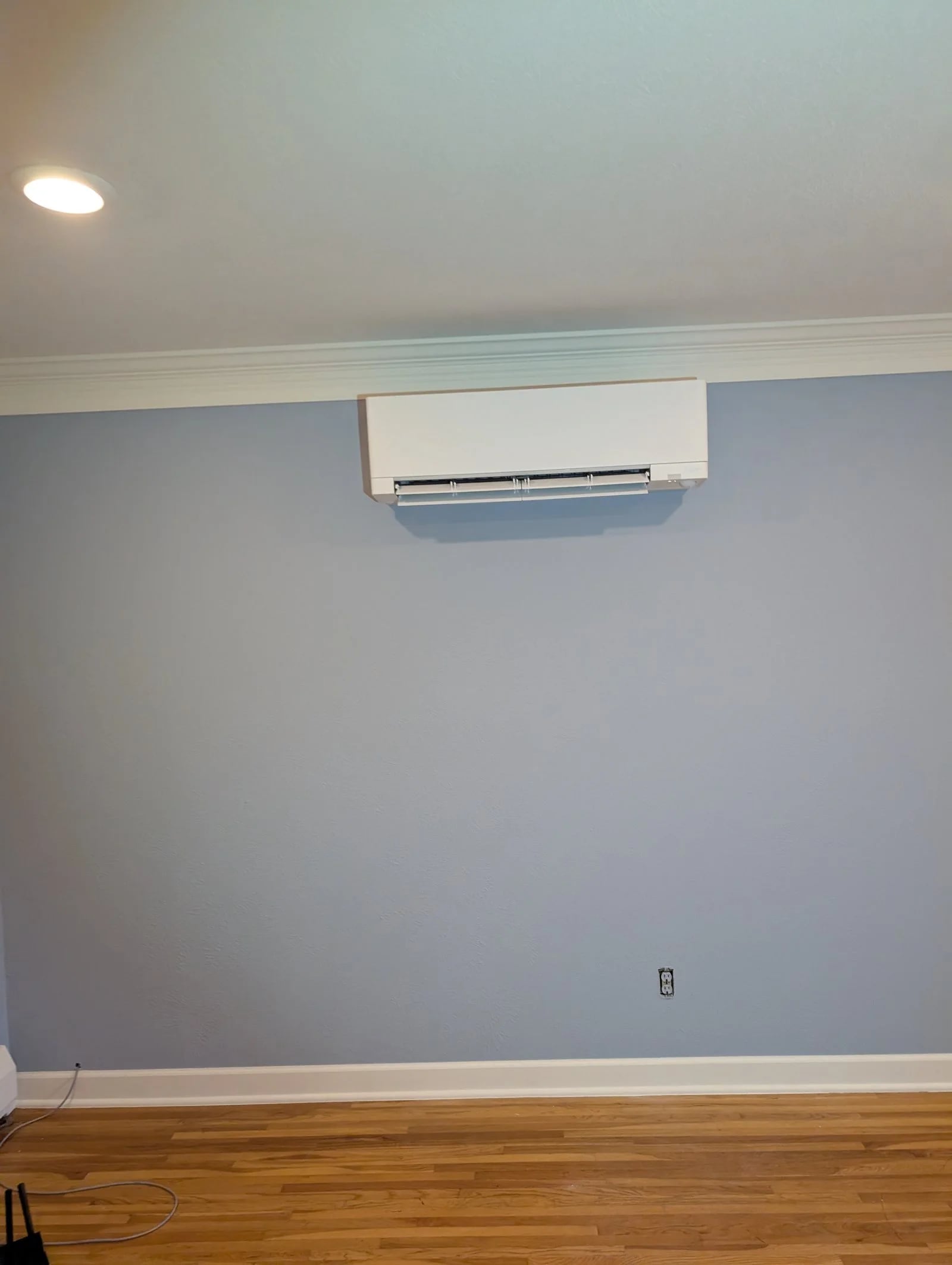 A ductless head on a blue-gray wall just below the crown molding, above a wood floor