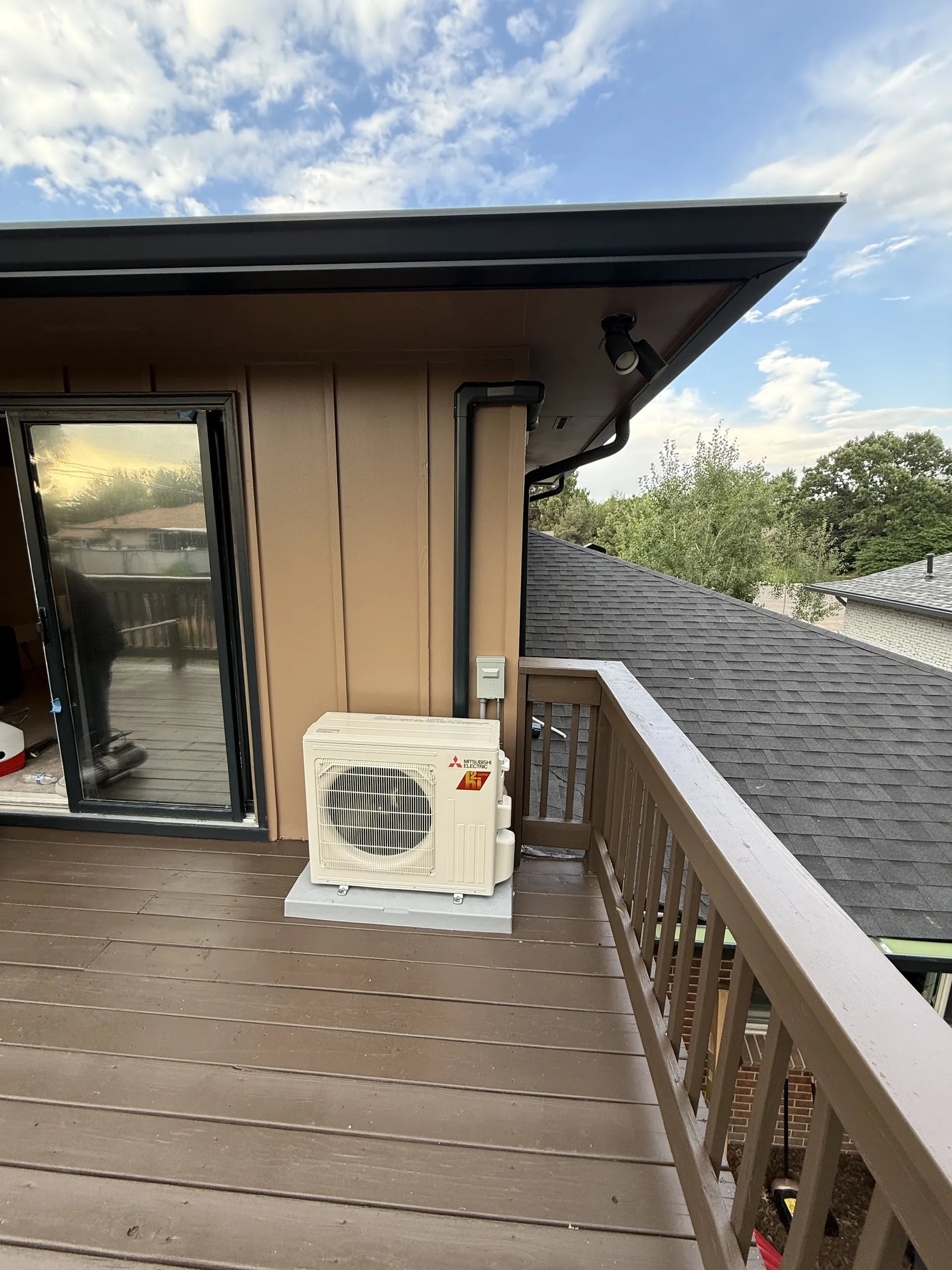 Mitsubishi compact outdoor unit on an upper wood deck with a railing and blue sky